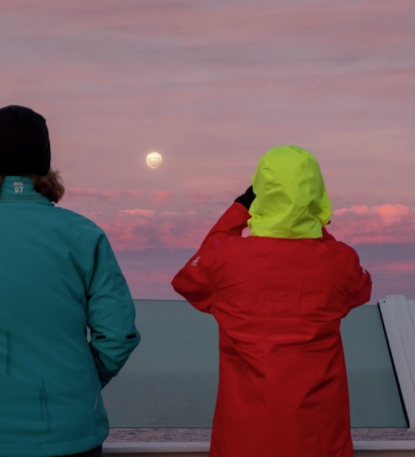To personer står og ser på solnedgang fra skipsdekk