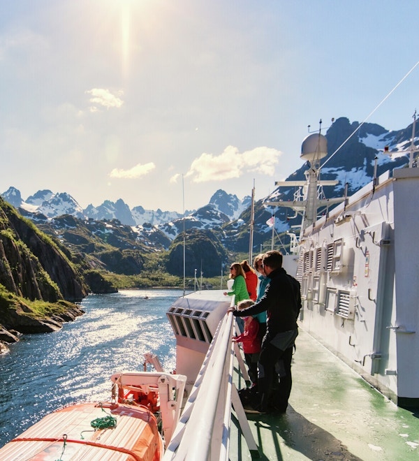 Folk står på skipsdekk og nyter utsikten til fantastisk fjellandskap.