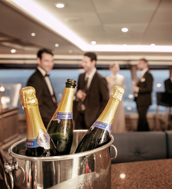 En champagnekjøler med tre flasker står foran festkledde mennesker