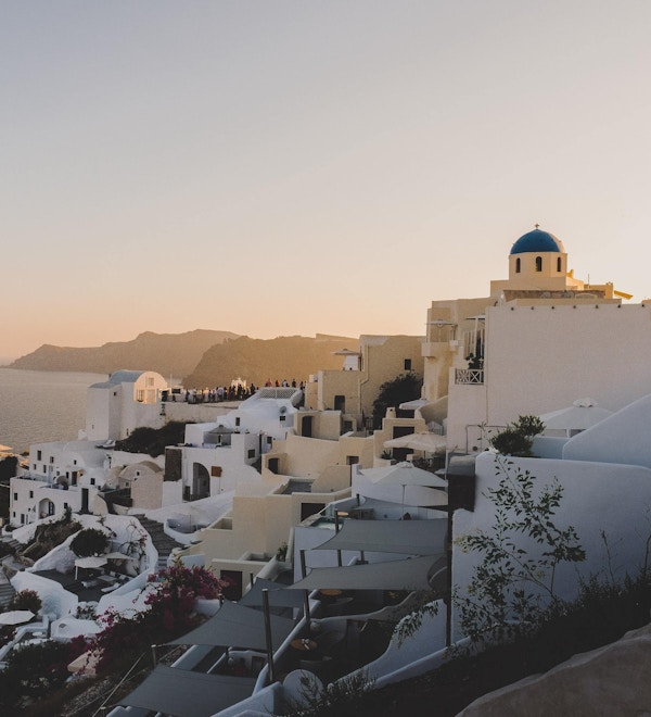 Utsikt over klassiske greske bygninger ved havet og en disig himmel i solnedgangsfarger