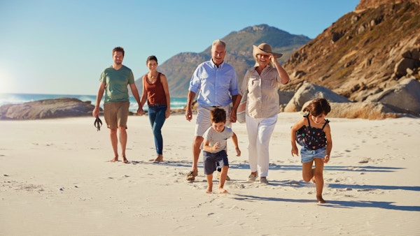 Tre generasjons familie som går sammen på en solrik strand, barn løper foran