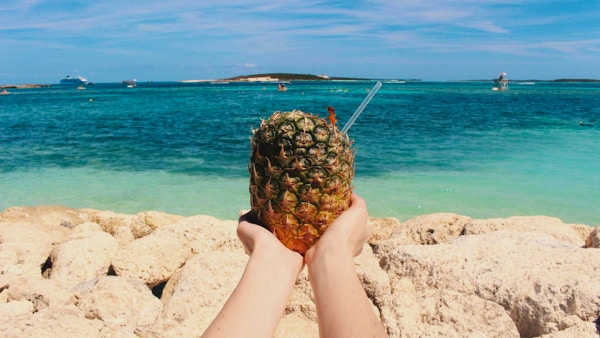 En fersk ananas på stranden holdes med begge hender mot havet