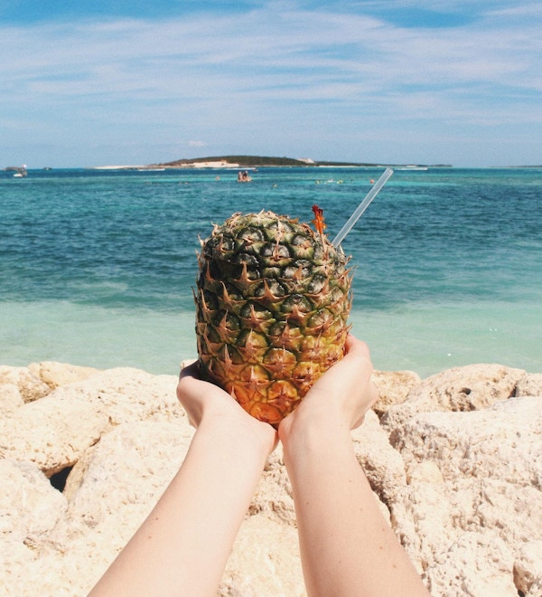 En fersk ananas på stranden holdes med begge hender mot havet