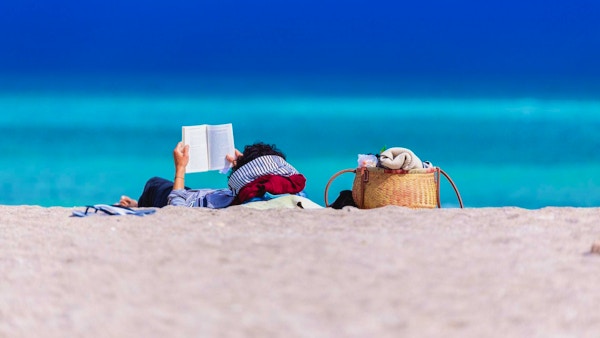 En rolig scene med en person som leser en bok på stranden.