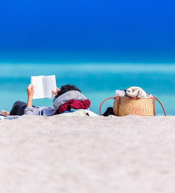 En rolig scene med en person som leser en bok på stranden.