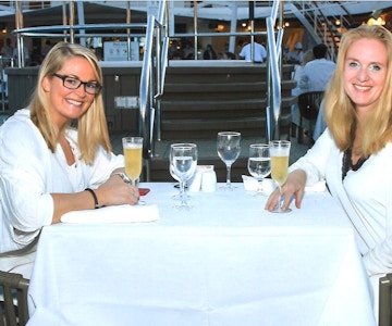 To damer drikker musserende vin, kledd i hvitt ved restaurantbord.