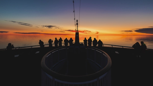 Passasjerer på dekk ombord på MS Roald Amundsen speider mot solnedgangen