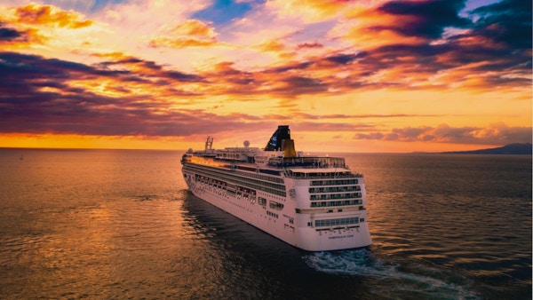 Stort hvitt cruiseskip seiler til havs i en fargerik solnedgang