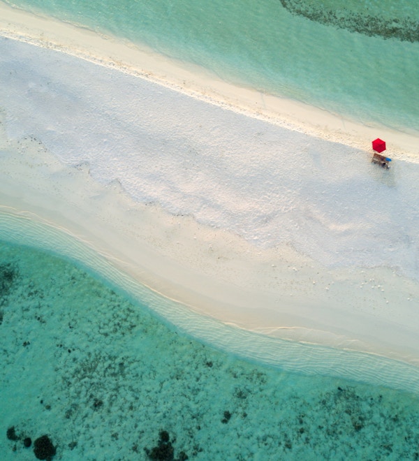 En ensom, rød paraply på den vakre stranden på en bitteliten øy i Sør Ari-atollen på Maldivene