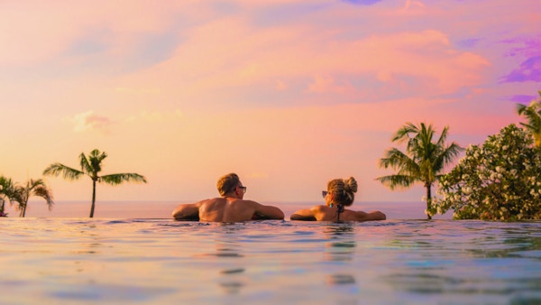 Romantisk kjærestepar som ser på en vakker solnedgang fra et svømmebasseng