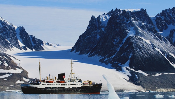 Skip foran arktisk landskap med spisse fjell.