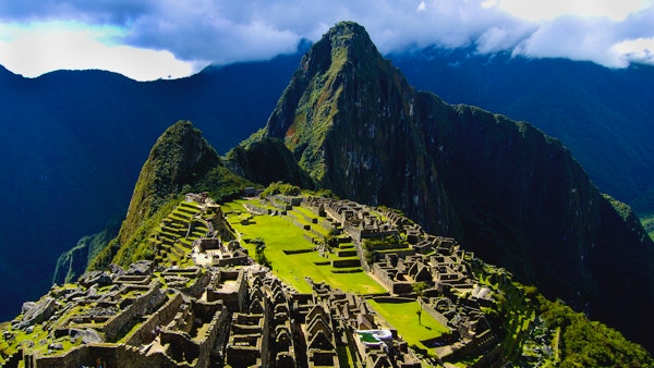 Solen skinner og lyser opp Machu Picchu i lys grønt mellom de gamle ruinene. Noen turister går i underverket