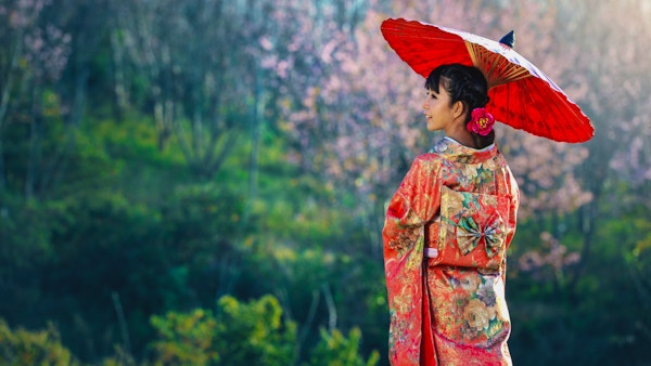 Kvinne kledd i kimono og med rød parasoll