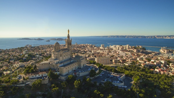 Høydevinkelsikt av bybildet ved sjøen. Notre Dame de la Garde i Marseille mot klar himmel. Bygninger ved sjølandskap på solrik dag.