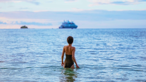 Kvinne bader med et cruiseskip i bakgrunnen