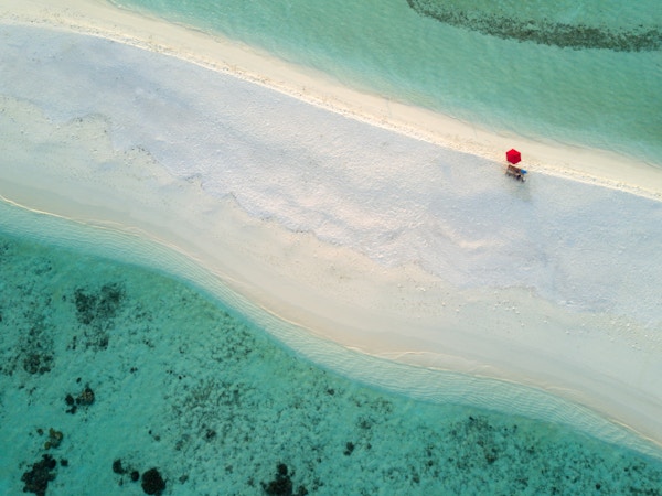 En ensom, rød paraply på den vakre stranden på en bitteliten øy i Sør Ari-atollen på Maldivene