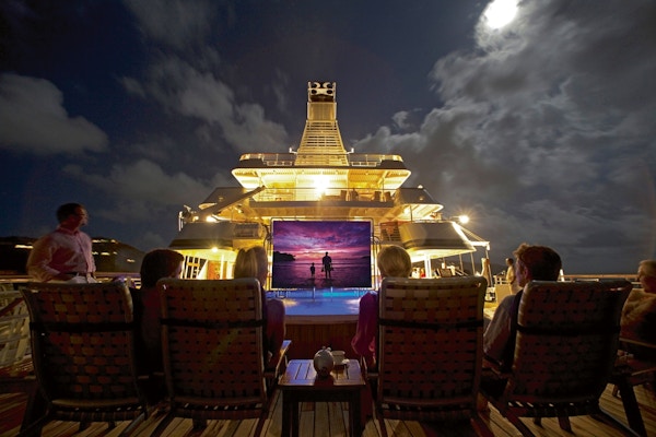 Kino på dekk av yacht om kvelden med tilskuere i behagelige stoler.