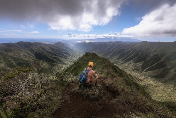 Mann sitter på toppet av et frodig fjell og ser på utsikten
