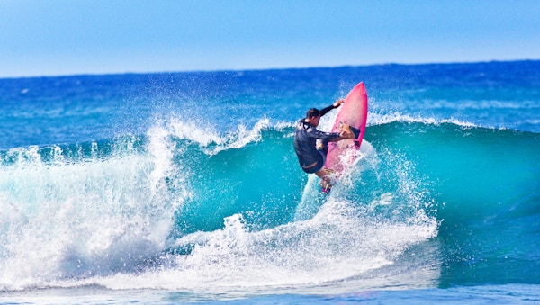 En ung, innfødt Hawaii-mann som surfer på bølgene utenfor Poipu Beach på øya Kauai, Hawaii, USA. Han er på et rosa surfebrett og gjør en sving på bølgen i havet utenfor Kauai.