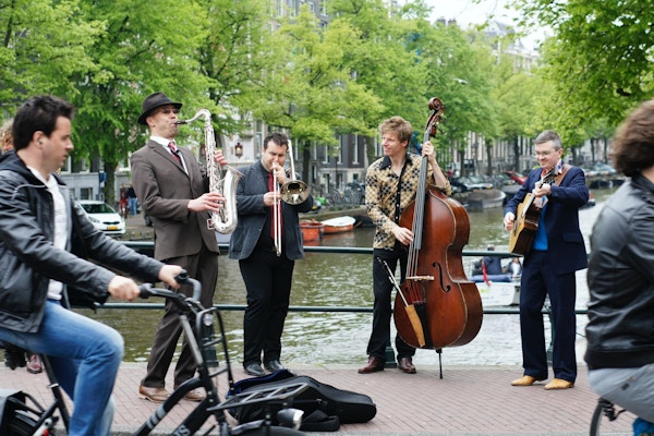 Fire musikere langs en kanal i Amsterdam, mens noen sykler forbi