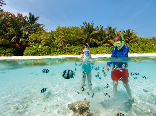 To barn med snorkleutstyr bader i krystallklart vann med tropiske fisker.
