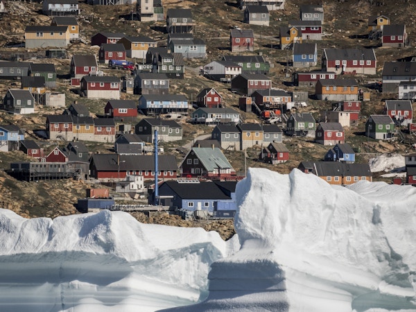 Tett bebygde fargerike hus i en fjellvegg med et stort isfjell i forgrunnen