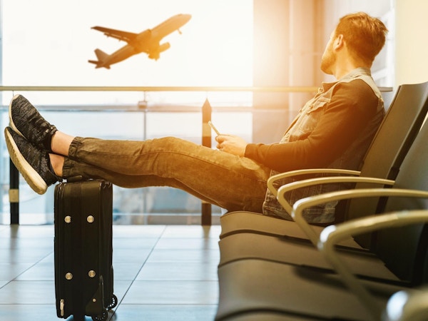 Mann sitter med beina på en koffert og venter, på en flyplass