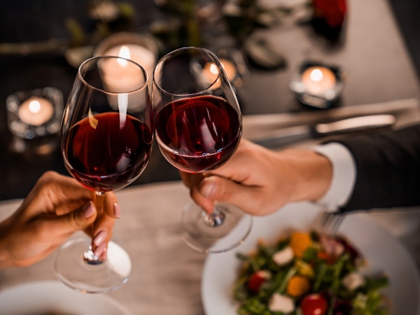 To hender skåler med rødvin over restaurantbord.