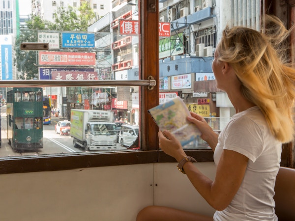 Ung turistkvinne som ser på et bykart på en trikk i Hong Kong..