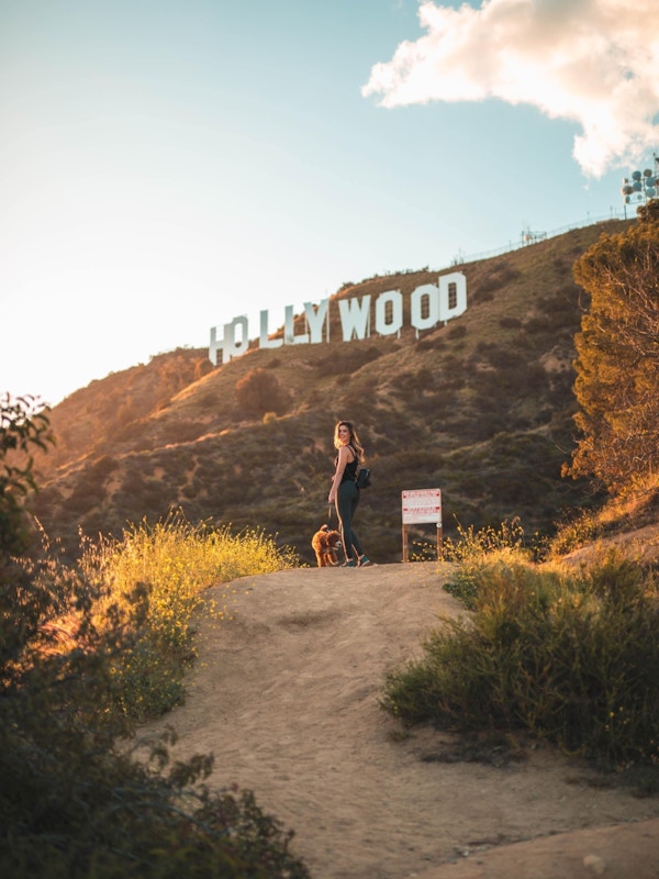Dame med hund på tursti med Hollywood-skiltet i bakgrunnen.