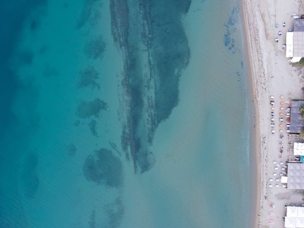 Luftfoto av en lys sandstrand og langgrunt hav