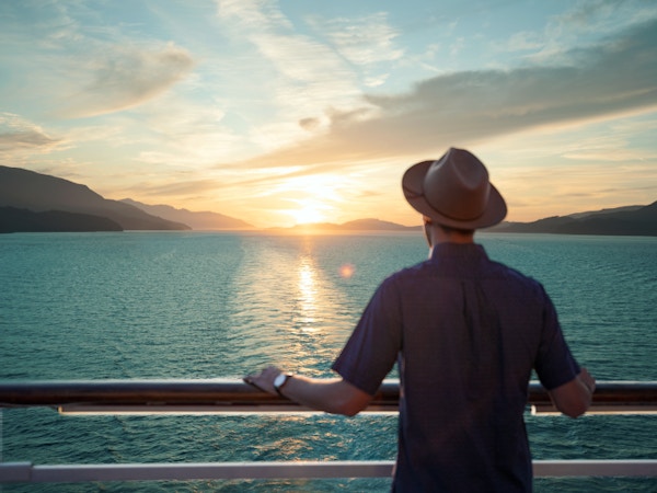Mann med hatt står ved rekka og ser på solnedgang
