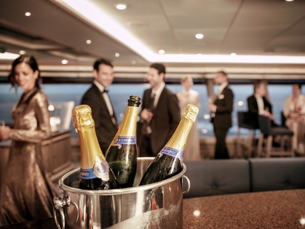En champagnekjøler med tre flasker står foran festkledde mennesker