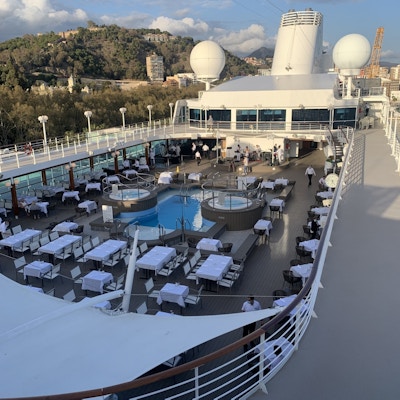 Dekk på cruiseskip med basseng og ferdig dekkede bord.