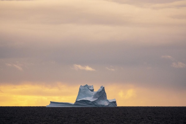 Isfjell i havet med kveldshimmel bak.