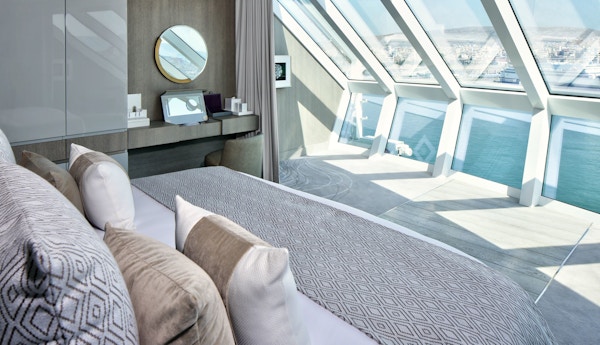 En herlig seng foran store vinduer i en suite om bord The Retreat