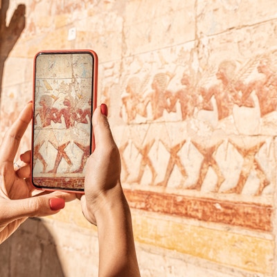 Reisebloggerjenta tar bilder på en smarttelefon ved de berømte freskene i Hatshepsut-tempelet i den gamle byen Luxor i Egypt. Eller ved hjelp av visuell turistguide