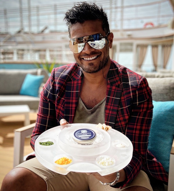 mann med solbriller holder opp et brett med kaviar og tilbehør