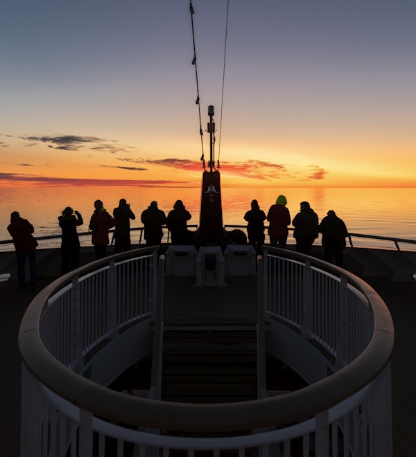 Passasjerer på dekk ombord på MS Roald Amundsen speider mot solnedgangen