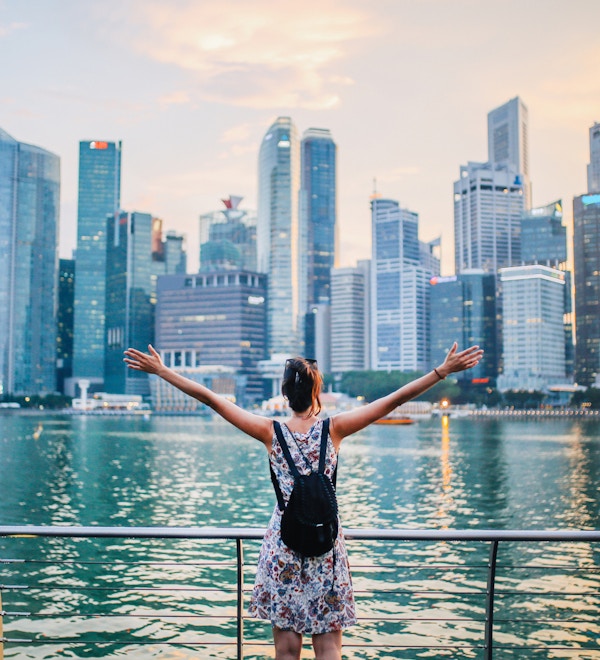 Ung reisende kvinne med armene utstrakt ser på solnedgangen over den fantastiske silhuetten i Singapore Bay-området. Frihet, reise, konsepter.