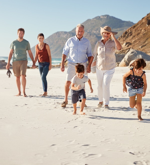 Tre generasjons familie som går sammen på en solrik strand, barn løper foran
