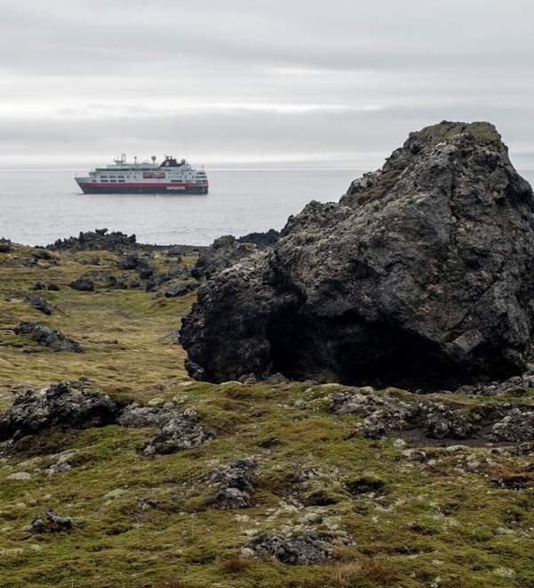 Landskapsbilde fra land med stor stein og havet med et skip utenfor