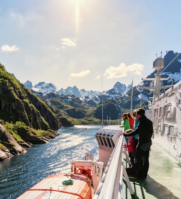 Folk står på skipsdekk og nyter utsikten til fantastisk fjellandskap.
