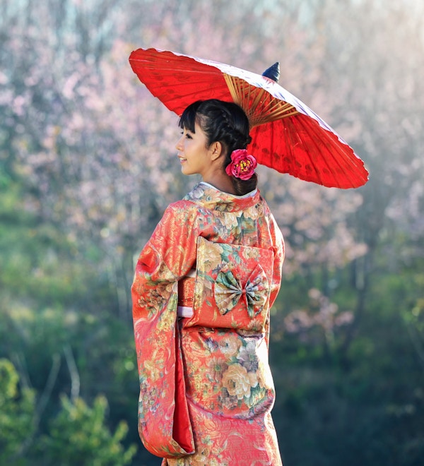 Kvinne kledd i kimono og med rød parasoll