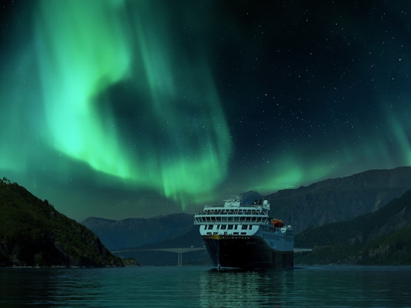 Skip på fjord med himmel full av nordlys i bakgrunnen.