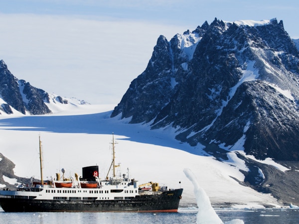 Skip foran arktisk landskap med spisse fjell.