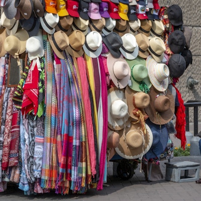 Kvinne ved markedsbod fylt av fargerike skjerf og hatter.