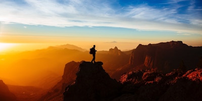 en person som står på toppen av et fjell ved solnedgang
